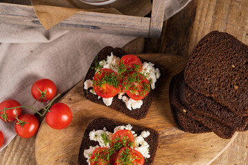 Black whole grain sliced bread with cottage cheese, tomatoes and dill on wooden rustic table. Country, organic dietic opened sandwich. Copy space. 