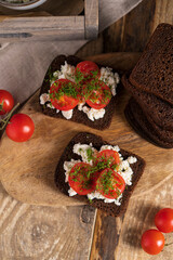 Black whole grain sliced bread with cottage cheese, tomatoes and dill on wooden rustic table. Country, organic dietic opened sandwich. Copy space. 