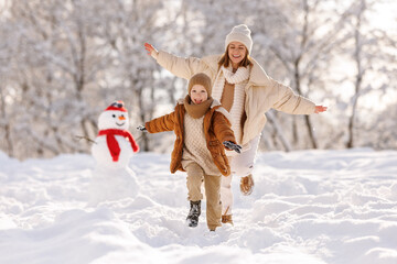Happy active family mother and little son have fun in winter park, play catch-up in snowy day