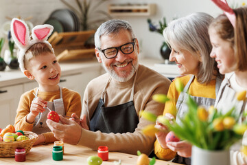 Happy little children creating beautiful painted eggs for Easter with loving senior grandparents