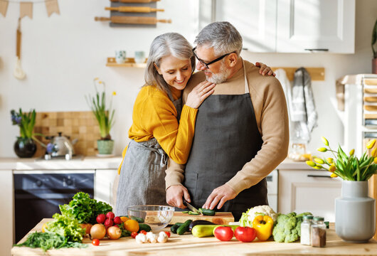Happy elderly couple in aprons cooking healthy food together in cozy kitchen at home