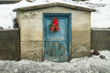 a town shed with peeling blue paint and a holiday evergreen wreath with a red bow
