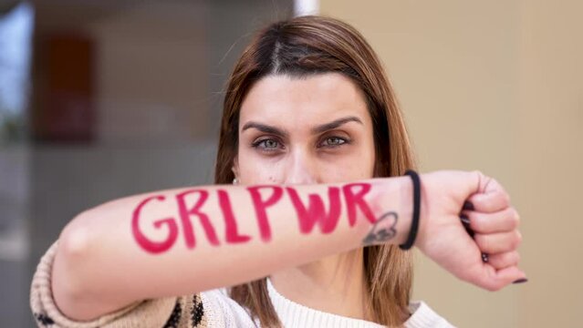 A young woman showing the letters "GLR PWR" written on her arm in slow motion