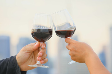 hands holding red wine glass on balcony during sunset, celebration concept