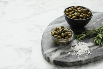 Delicious pickled capers, salt and rosemary twigs on white marble table, space for text