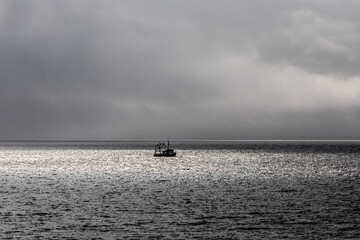 An inshore fishing boat caught in a patch of sunlight on a cloudy day in Ardnacross Bay on the Kintyre Peninsula, Argyll & Bute, Scotland UK
