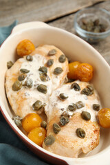 Delicious chicken fillets with capers, tomatoes and sauce in baking dish on table, closeup