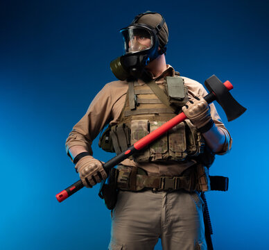 a soldier in military clothes with a bulletproof vest in a gas mask holds a red fire axe in his hands