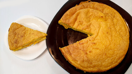 Delicious cottage cheese and pumpkin casserole with a cut off piece on a black square plate as if eating itself on a white background