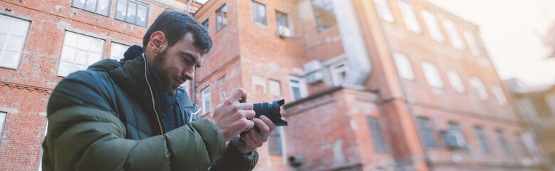 Portrait of a young male photographer with a camera takes a photo or video on the street, in an old...