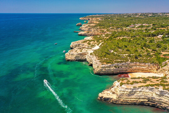 Aerial view of boats cruising along the turquoise waters of the rocky coastline of Albufeira, Algarve, Portugal.