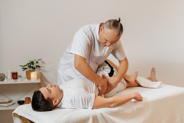 Strong and concentrated masseur therapist in uniform making manual therapy for athlete back. Professional massage treatment and rehabilitation for sportsmen. Concept of wellness, body and health care.