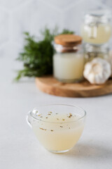 Bone broth in a mug with spices, broth in storage jars and a bunch of fresh dill in the background. 