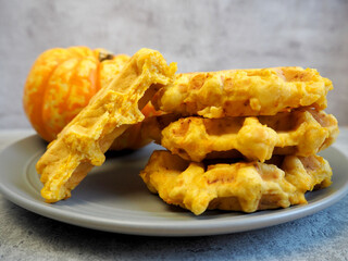 gluten-free and lactose-free belgian waffles with pumpkin stand on a gray plate with a small pumpkin on a gray table 