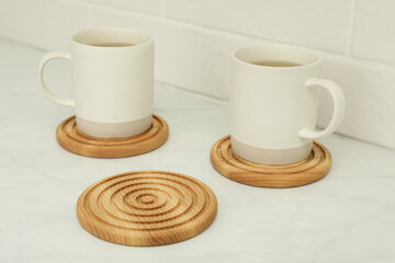 Hot beverage in mugs and stylish wooden cup coasters on white table