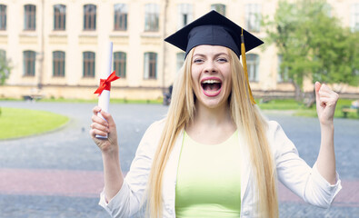Portrait of a happy and excited young woman student in a graduation hat on the background of the...