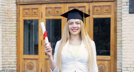 Happy young woman student in a graduation hat on the background of the university. Completion of...