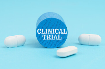 Pills lie on a blue surface, a wooden blue cylinder with the inscription - CLINICAL TRIAL