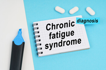 On a white and blue surface are pills, a marker and a notebook with the inscription - Chronic fatigue syndrome