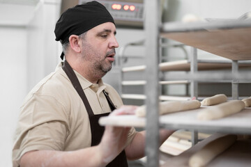Baker placing tray with formed raw dough on rack trolley ready to bake in the oven. High quality photo