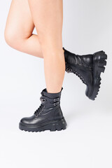 Legs of a woman in black leather boots from a new collection on a white background, legs of a girl in fashionable leather boots spring 2022.