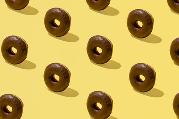 Chocolate glazed donuts pattern against vanilla yellow background. Summer mood, fast food idea. 