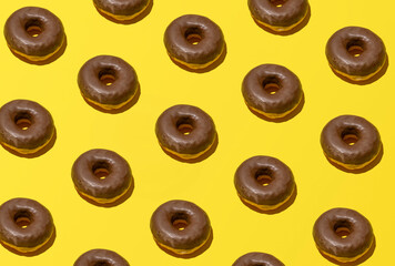 Chocolate glazed donuts pattern against vanilla yellow background. Summer mood, fast food idea. 
