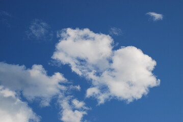 A small white cloud in a clear blue sky. Small cumulus clouds float across the light blue sky. They form a small group next to each other. Clouds of various shapes and sizes.