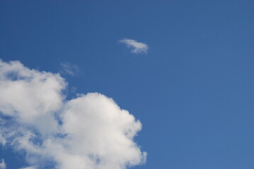 White clouds in a clear blue sky. Small cumulus clouds float across the light blue sky. They form a small group next to each other. Clouds of various shapes and sizes.