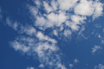 A small white cloud in a clear blue sky. Small cumulus clouds float across the light blue sky. They form a small group next to each other. Clouds of various shapes and sizes.