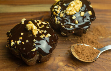 Two chocolate brownies on a wooden table next to a spoonful of chocolate powder
