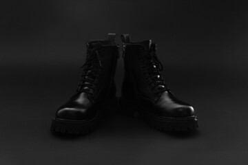 Pair of glittering isolated leather winter autumn unisex black boots on bright black background. Boots with block heel, round toe and embossed hard sole. Copy space.