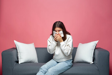 Sick young girl blow runny nose, sneeze, suffer from allergy, flu or cold, sitting on sofa on...