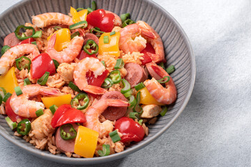 Jambalaya rice with chicken, shrimp, sausage and vegetables in plate on gray concrete table