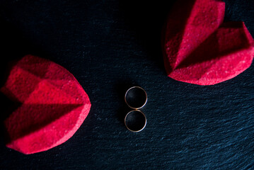 On Valentine's day or wedding two red hearts and rings lying on black surface