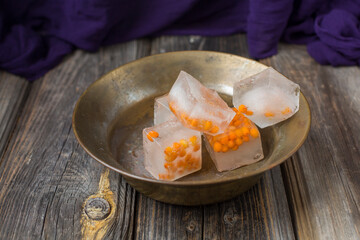 Sea buckthorn frozen in pieces of ice in vintage bowl. Textured background, wooden , purple color