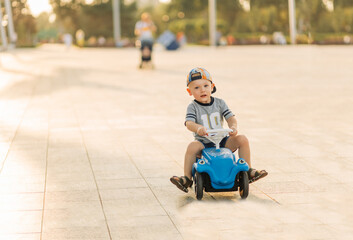 child with a toy car outdoors. The boy rides on a typewriter in the park.Active rest with children on a warm summer day.