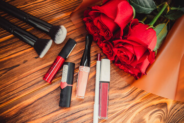Obraz na płótnie Canvas Beautiful bouquet of red roses on a brown background with makeup brushes and lipsticks