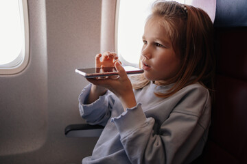 a little girl is talks hands-free calls on the phone in an airplane seat