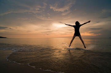 A young woman doing a star jump, enjoying her freedom on the beach at sunset., Thai Islands at Koh Samui, Thailand, Southeast Asia