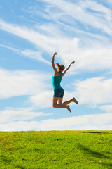 Happy woman jumping for joy, celebrating winning and enjoying happiness of freedom and carefree lifestyle on green grass with blue sky, background with copy space