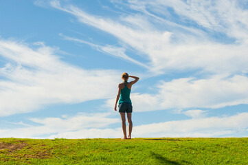 Woman standing, looking at a view with hope towards the future in a rural scene of green grass and blue sky, background with copy space