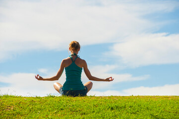 Peaceful woman meditating in a tranquil scene, enjoying spirituality in rural landscape scenery of green grass with blue sky, background with copy space