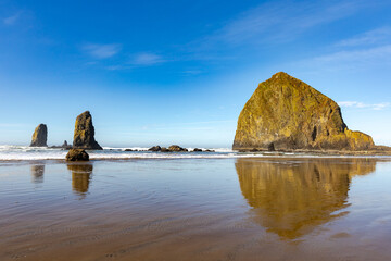 Fototapeta na wymiar Haystack Rock in Cannon Beach, Oregon, with rocky coastline on a clear, blue sky afternoon.