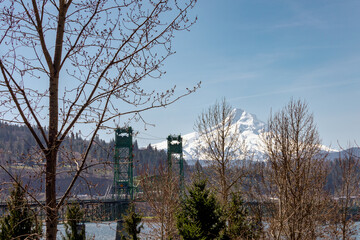 Distant beautiful view of snow capped Mount Hood in Oregon, with Bridge of the Gods in the foreground alongside  autumn trees and bare branches with pale blue sky.