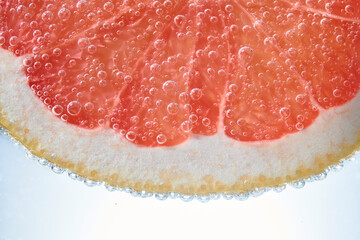 Red grapefruit slice floating in club soda. Fresh citrus slice with bubbles in carbonated drink. Fresh natural soft drink orange citrus flavour. 