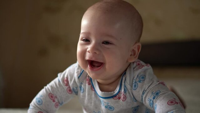 Newborn Active Baby Cute Smiling Teethless Face Portrait Early Days On Stomach Developing Neck Control. 5 Months Child On White Bed Looking on Camera. Infant, Childbirth, Parenthood, Beginning Concept