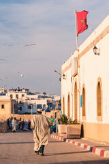 Moroccan man walking through Essaouira under the Moroccan flag to Moulay Assan Square, Morocco,...