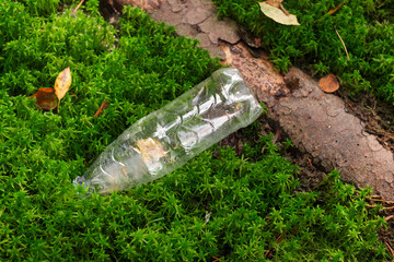 An empty plastic bottle thrown by people in the forest moss lies next to a log. Pollution of the surrounding land. Harm and huge damage to the planet. The concept of environmental protection. 