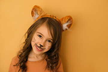 A nice smiling girl with a tiger mask pattern on her face and a headdress with ears looks sweetly...